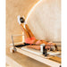 AussiePilatesCoastAP-01HomeReformerInCreamColourandFemaleUsingItwithsoftballbetweenfeet