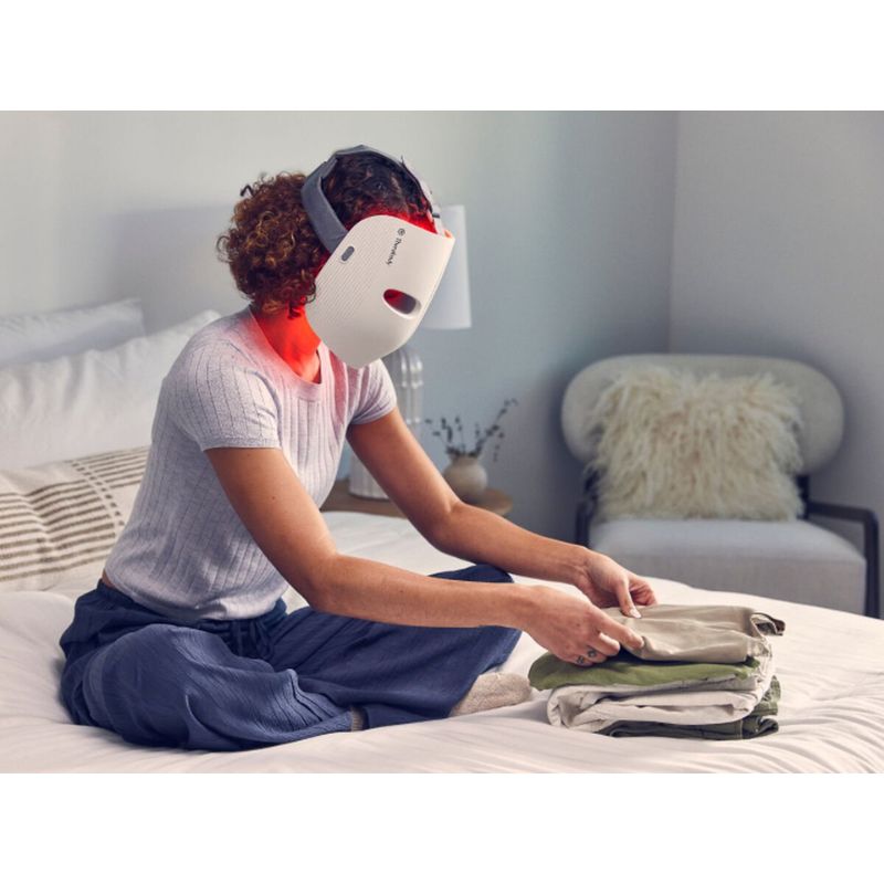 TherabodyTheraFaceWhiteLEDMaskwithfemaleusingitwhilefoldingclothes